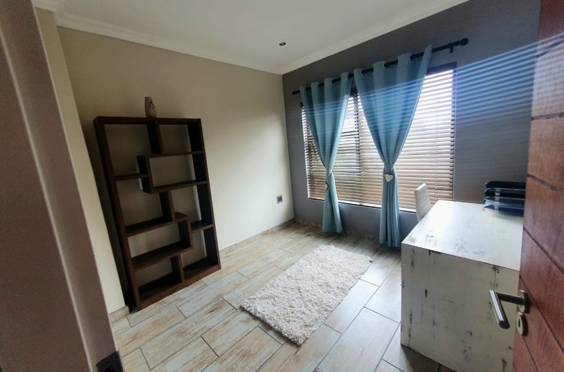 Second bedroom or study, with tile floor, big window with blinds and blue curtains. Interior of a townhouse that is for sale in The Villas, Glen Eagle Estate, Kempton Park.