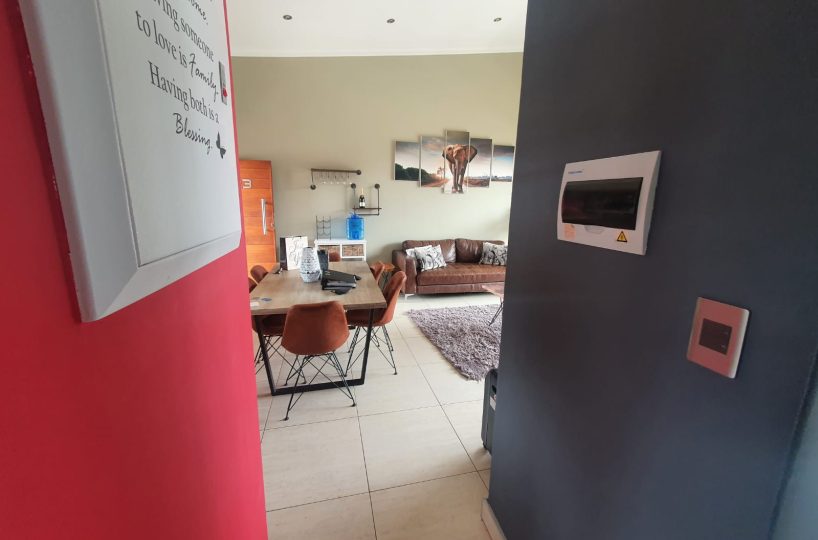 Interior of a townhouse that is for sale in The Villas, Glen Eagle Estate, Kempton Park. View into the living area with a dining table. Piture is framed by blue and red accent walls. Ther is a picture of an elepahnt on the far wall.