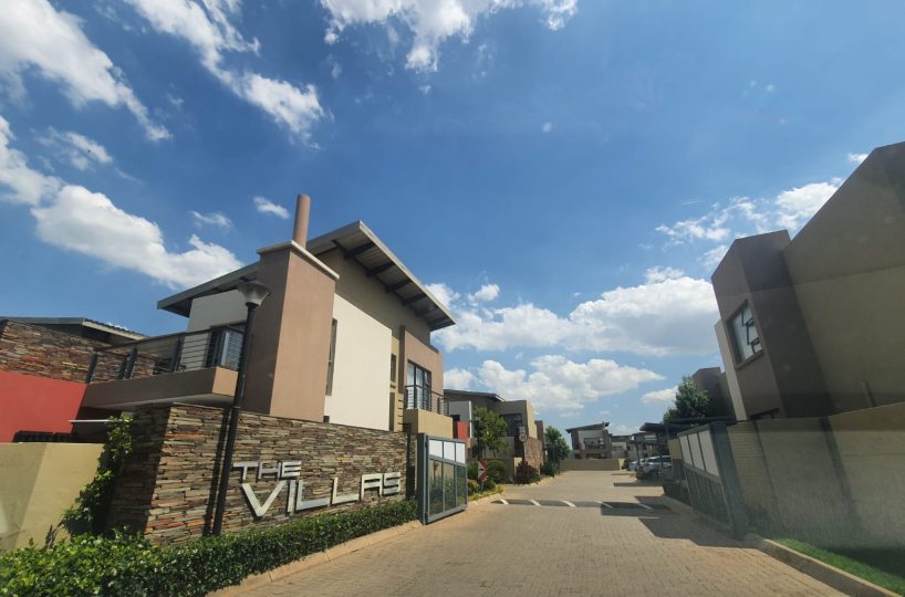 Outside view of the Villas complex gate with a townhouse that is for sale in The Villas, Glen Eagle Estate, Kempton Park. The sign that says the Villas is visible on a rock claded wall in silver letters.
