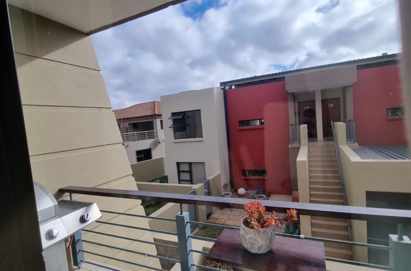 View from balcony of a townhouse that is for sale in The Villas, Glen Eagle Estate, Kempton Park. The railing is made of steel with wood on top. The floor is tiled. It overlooks another block in the complex.