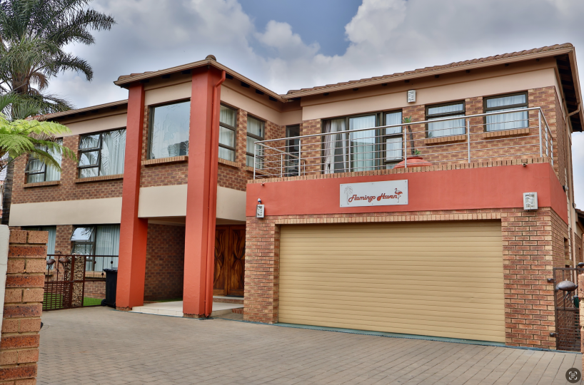 Double story facebrick house from front with blue sky and clouds. Property for sale in Kempton Park. It has orange pillars and a yellow garage door with paving in front