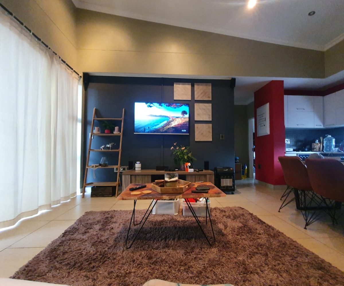 Interior of a townhouse that is for sale in The Villas, Glen Eagle Estate, Kempton Park. A open plan living area with a sloping ceiling, dark blue, red and neutral walls. It is furnished with medern furniture and the kitchen is visible to the right.